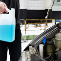 Person holding bottle of windshield washer fluid in front of an open car hood